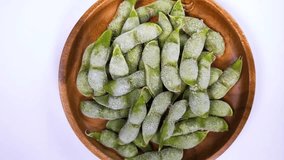 Frozen boiled Edamame (green soybeans) in a wooden bowl on white background rotating - Powered by Shutterstock - Get 15% off with code: PIKWIZARD15