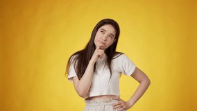 Thoughtful casually dressed young woman with long dark hair with forefinger touching chin while thinking as if weighing different options against amber background - Powered by Shutterstock - Get 15% off with code: PIKWIZARD15