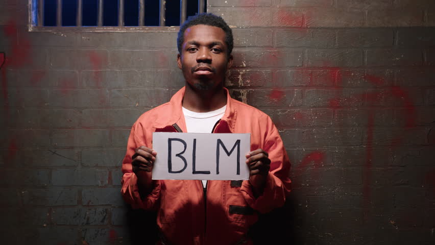 African American prisoner with poster with abbreviation BLM against brick wall
