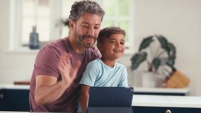 Mature father in kitchen at home with son sitting at counter making video call on digital tablet - shot in slow motion - Powered by Shutterstock - Get 15% off with code: PIKWIZARD15