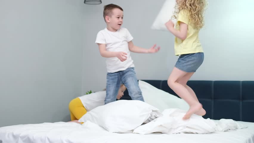 four little kids two boys and two girls brothers and sisters merrily jumping on the beds of their parents' bedrooms bouncing, fooling around pillow fight at home. happy children. slow motion Royalty-Free Stock Footage #1106970241