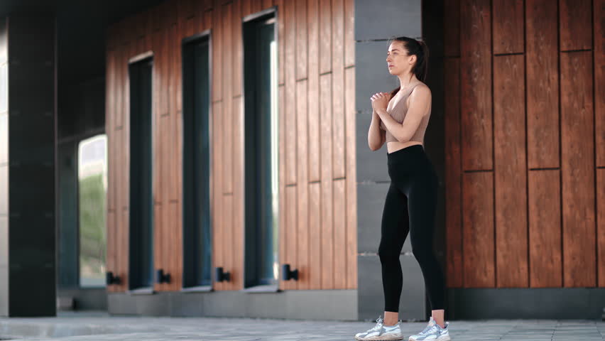 Fitness woman training outdoor doing squat buttock legs exercising workout at modern building exterior. Sport female performing training exercise in squatting position body care physical activity Royalty-Free Stock Footage #1106977915
