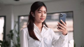 Video call, a young Asian woman communicates via smartphone wearing earbud having chat