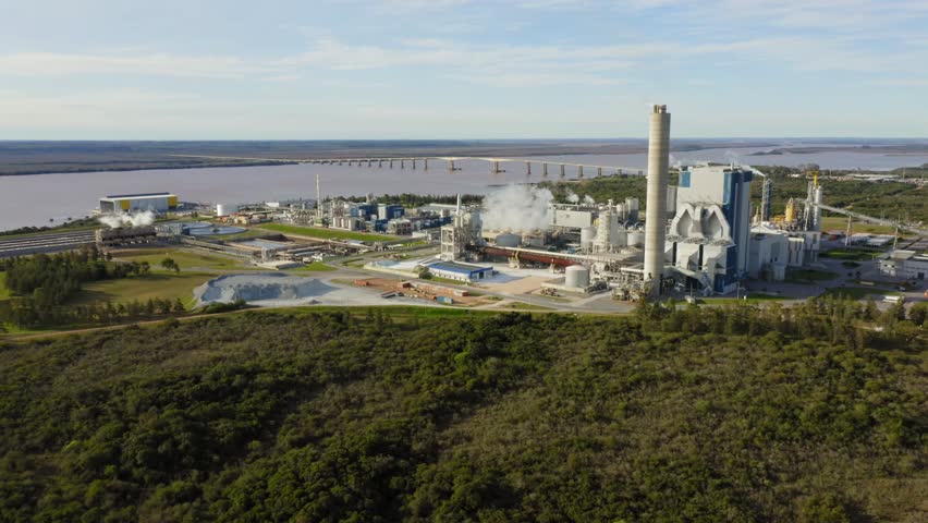 Pulp mill on river bank in Uruguay South America. Factory manufactures bleached hardwood eucalyptus pulp. Static aerial view. Royalty-Free Stock Footage #1106983911