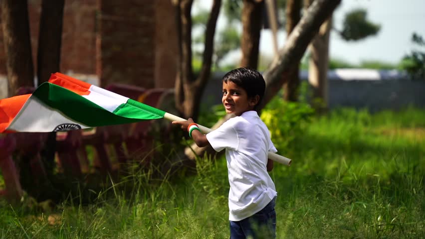 Cute little boy holding Indian flag in his hands and smiling. Celebrating Independence day or Republic day in India. A boy showing pride of Tiranga