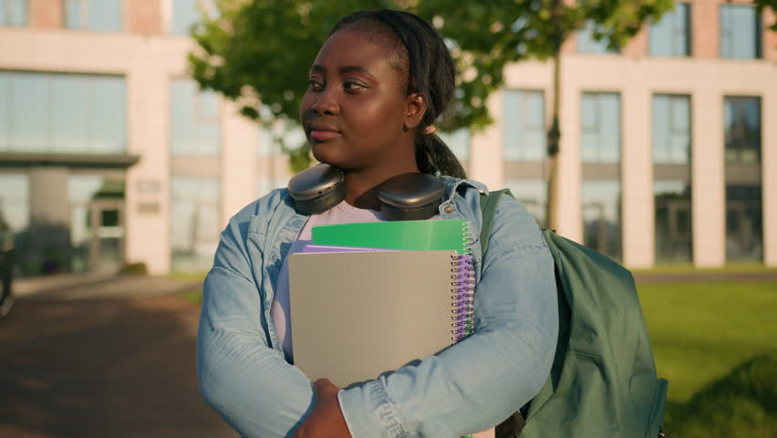 Portrait African American woman university college campus academy student teen girl high school pupil holding books with schoolbag headphones smiling toothy joyful in city outdoors study education Royalty-Free Stock Footage #1106991463