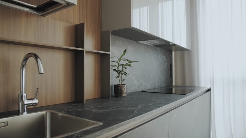 Kitchen sink and faucet, interior supplemented with plants. Simple well designed modern kitchen interior.Black ceramic tiles on the wall and countertop and wooden facade, slow motion shot.