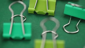 closeup multicolored bright metal paper clips rotate on a green background. a collection of stationery for office documents and administration.
