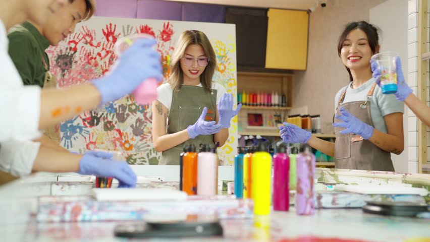 Group of Asian generation z people learning acrylic pouring art on canvas workshop at art studio. Young artist university student enjoy and fun creating colorful abstract modern art painting in class.