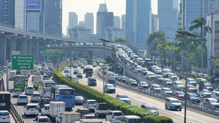 Many vehicles pass by in heavy traffic and are jammed on Jakarta's urban roads and bridges. Depicts traffic congestion, chaos and heavy pollution. Shot with a telephoto lens during the day. Royalty-Free Stock Footage #1107000605