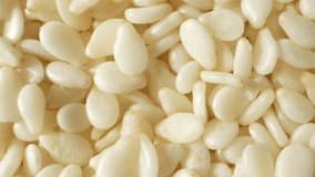 White sesame seeds, They have a flattened teardrop shape, with one end pointed and the other slightly broader. The seeds' color is a pale, creamy white, and their outer surface is smooth and shiny.