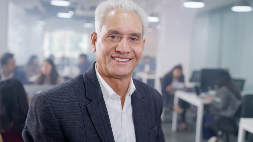 Track back shot Smiling confident happy Indian Asian male old corporate business entrepreneur or senior with boss arms crossed and looking at the camera with busy office employees working in the back Royalty-Free Stock Footage #1107004479