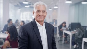Track back shot Smiling confident happy Indian Asian male old corporate business entrepreneur or businessman with arms crossed and looking at the camera with busy office employees working in the back - Powered by Shutterstock - Get 15% off with code: PIKWIZARD15