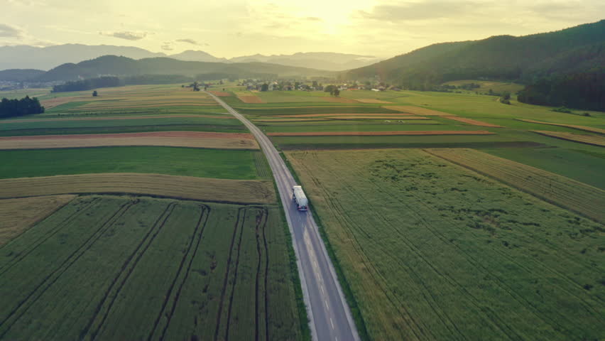 Lorry truck driving along countryside highway, transporting liquid cargo aerial view tracking shot. Oil tanker riding on road at sunset with mountains on horizon Royalty-Free Stock Footage #1107005155