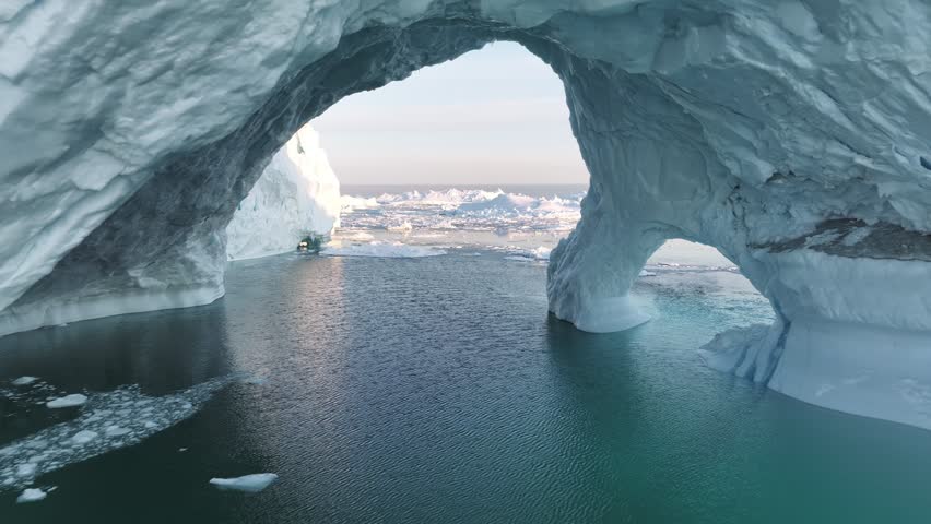 Flying inside ice cave. Gaint iceberg with ice cave melting in the ocean. Icebergs from melting glacier float in Disco Bay, near Ilulissat, Greenland. Aerial shot, climate change concept Royalty-Free Stock Footage #1107006361