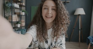 Portrait of excited young woman making video call talking online waving hand looking at camera at home. Communication and emotion concept.