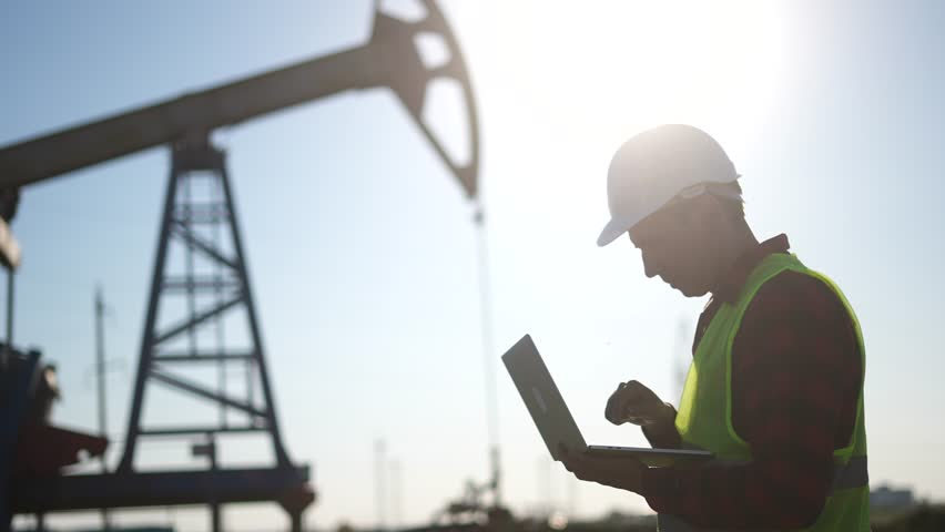 oil business. a worker works next to an oil pump holding a laptop. industry business oil and gas lifestyle concept. engineer studying the level of oil production on a laptop silhouette at sunset Royalty-Free Stock Footage #1107008831