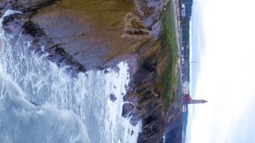 Coastal lighthouse. Aerial towards Waves crash over rocks aerial over island with lighthouse. Aerial fly over coastal lighthouse with waves crashing on the cliffside. Portugal. Aerial vertical video.  - Powered by Shutterstock - Get 15% off with code: PIKWIZARD15
