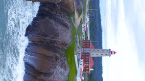 Coastal lighthouse. Aerial towards Waves crash over rocks aerial over island with lighthouse. Aerial fly over coastal lighthouse with waves crashing on the cliffside. Portugal. Aerial vertical video.  - Powered by Shutterstock - Get 15% off with code: PIKWIZARD15