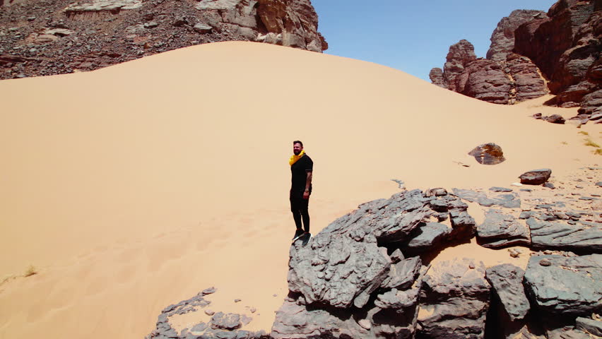 Tourist Man Standing On Edge Of A Cliff In Djanet Desert In Algeria - drone shot