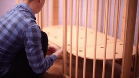 Man fixing wooden  crib bed, preparation for the appearance of a newborn child.Bolting process. Making the bed horizontal 4k footage