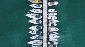 Flying over a marina with boats and yachts. Aerial top view of Luxurious boats are moored at the pier, slowly swaying on the waves.