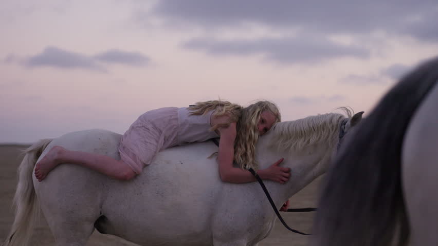 A girl tenderly embraces a majestic white horse showing love and trust, while another horse