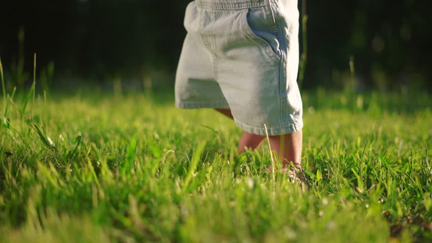 baby first steps. happy family kid dream concept. baby walks on the grass learns to walk in the city park close-up. baby lifestyle first steps in nature. dad teaches son to walk Royalty-Free Stock Footage #1107032751