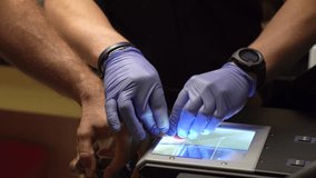 A security man with gloves taking fingerprints of a person on a scanning device - Powered by Shutterstock - Get 15% off with code: PIKWIZARD15