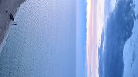 VERTICAL VIDEO, Small wooden fishing boat on a sandy beach at sunset, sea horizon