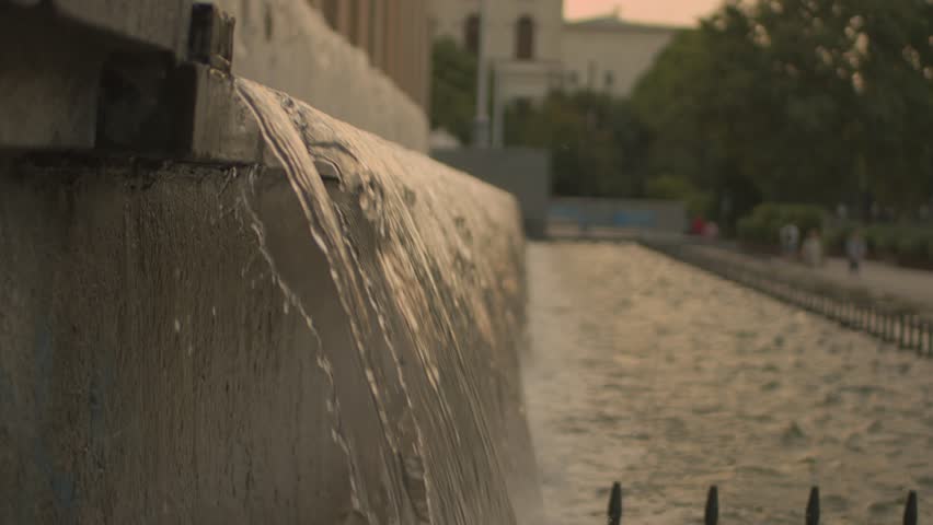 Fountain near a granite building, water pours in a long wave, cloudy day, no one