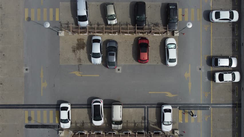 Aerial view of parked vehicles and people walking in a large car park, there are places reserved for the disabled in the parking lot