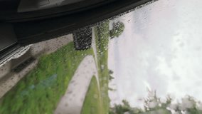 Vertical video. View of the green rural landscape from the driving car. Raindrops on the window. Driving along the road in the countryside at summer rain, view of green grass and trees