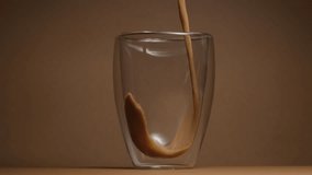 Front view of coffee liquid is flowing down a glass on a brown background. Coffee cup pour slow motion. High quality footage for instant coffee or instant coffee product ads