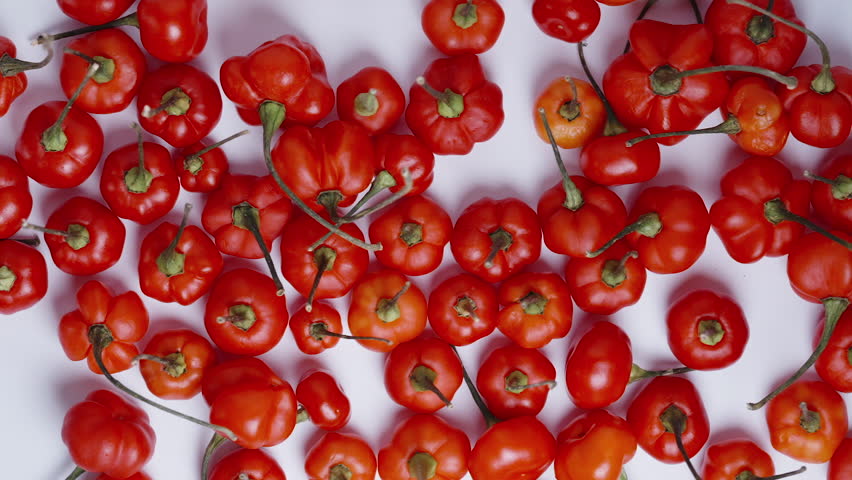 Slow-motion close-up view of yellow Habanero peppers falling onto red mini peppers of The Star of Turkey from above.