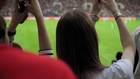 A view from the back of women in the stands of a football stadium, they take photos on their phone. Football fans in the stands of the stadium during a football match. - Powered by Shutterstock - Get 15% off with code: PIKWIZARD15