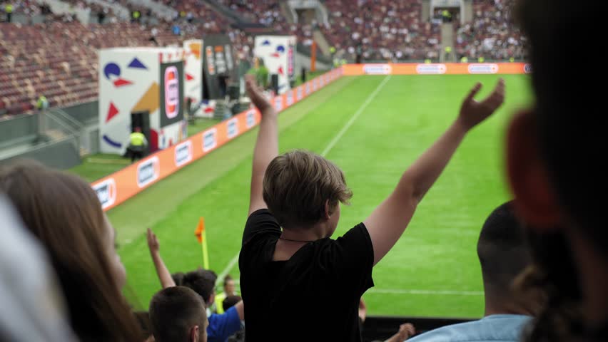 The silhouette of a teenage boy at a football match, he stands with his hands raised and claps. Football fans in crowded stands. Royalty-Free Stock Footage #1107053217