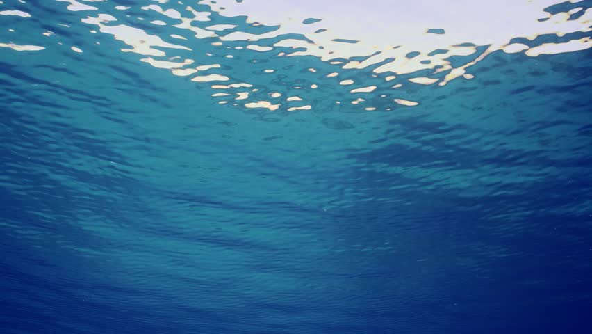 Small swell on surface of Ocean, Slow motion. Surface of water during calm on bright sunny day. Underwater view of calm blue water surface. Natural blue water backgroundv