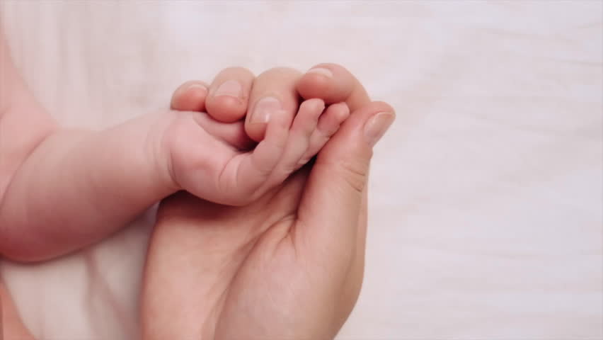 Close up above view loving young mommy holds hand of her newborn while baby lying on comfortable white bed at home. Cherish, mothers love and care, protection of children, adoption, babyhood concept Royalty-Free Stock Footage #1107057485