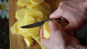 Woman cuts potatoes over the cutting board on the table, close-up, video