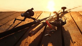 Two fishing spinning rods with fishing tackles lie on a wooden pier against the backdrop of a sunset over a lake or river or sea. Fishing background, stock video 4k. Fishing concept