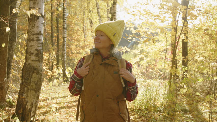 Happy woman walking in autumn park with yellow foliage on sunny day.