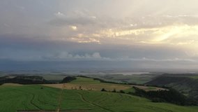 Drone panoramic view of São Paulo highlands, with the Tietê river underneath storm clouds on the back and vast sugar cane plantations surrounded by forests on the front, composed with fantastic sunset