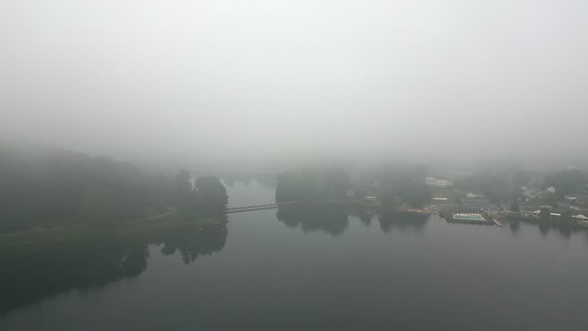 Aerial flyover: Pedestrian foot bridge on foggy rural lake on calm day
