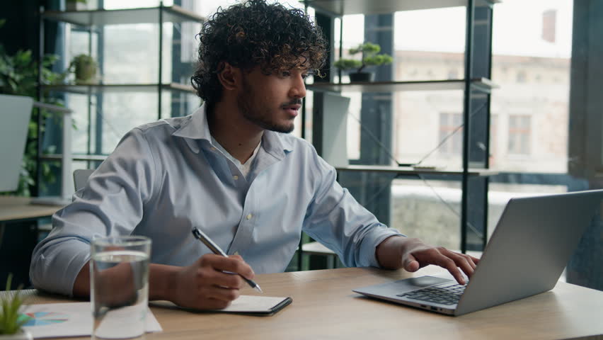 Arabian Indian latin man businessman guy write business notes ideas in notebook managing corporate tasks writing schedule with pen on desk male worker employee working with laptop computer in office Royalty-Free Stock Footage #1107068699