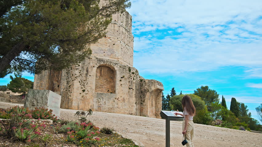Beautiful girl reading the label of Tour Magne in Nimes, France. Tourist consults the map guide of the watchtower stone, part of the Roman city wall from the Augustinian era, with panoramic views.
