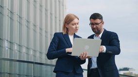 Gimbal shot two business partners caucasian man woman in formal suits standing outdoors office building terrace discussing upcoming project and deals using laptop. Corporate employees in downtown city - Powered by Shutterstock - Get 15% off with code: PIKWIZARD15