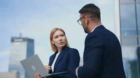 Handheld portrait shot two business partners bearded man blonde woman standing outdoors office building terrace or balcony discuss upcoming project deals using laptop. Corporate people city downtown - Powered by Shutterstock - Get 15% off with code: PIKWIZARD15