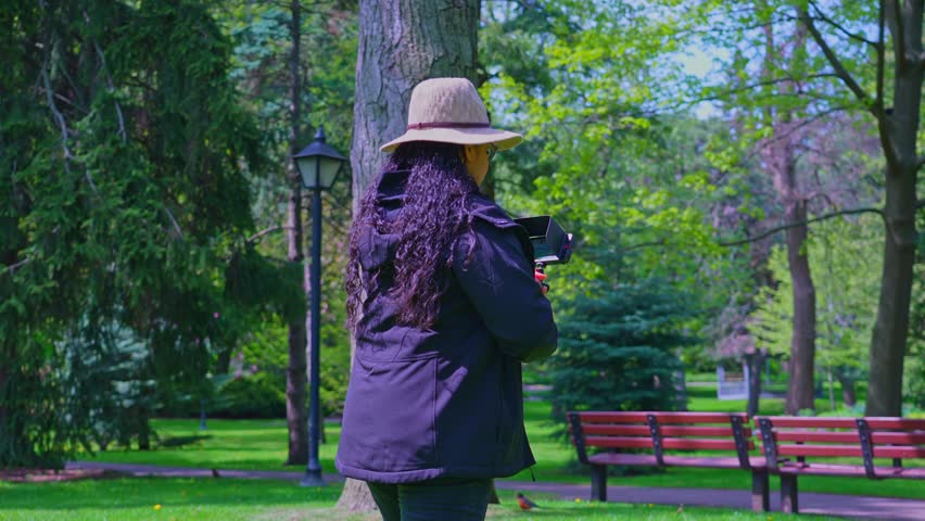 Middle age woman photographer or videographer with a camera rig set up in her hands shoot content in the nature forest park. Female nature photographer taking picture with camera in the flowers garden