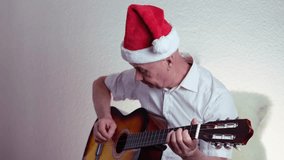middle-aged man in santa claus hat plays acoustic guitar christmas music, teacher teaches how to play musical instrument, blogger performance, concept of christmas, silvester, waiting for holiday